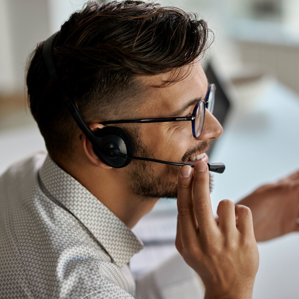 Ein lächelnder Mann von der Seite fotografiert, mit einem Headset auf dem Kopf und der Hand am Mikrofon.